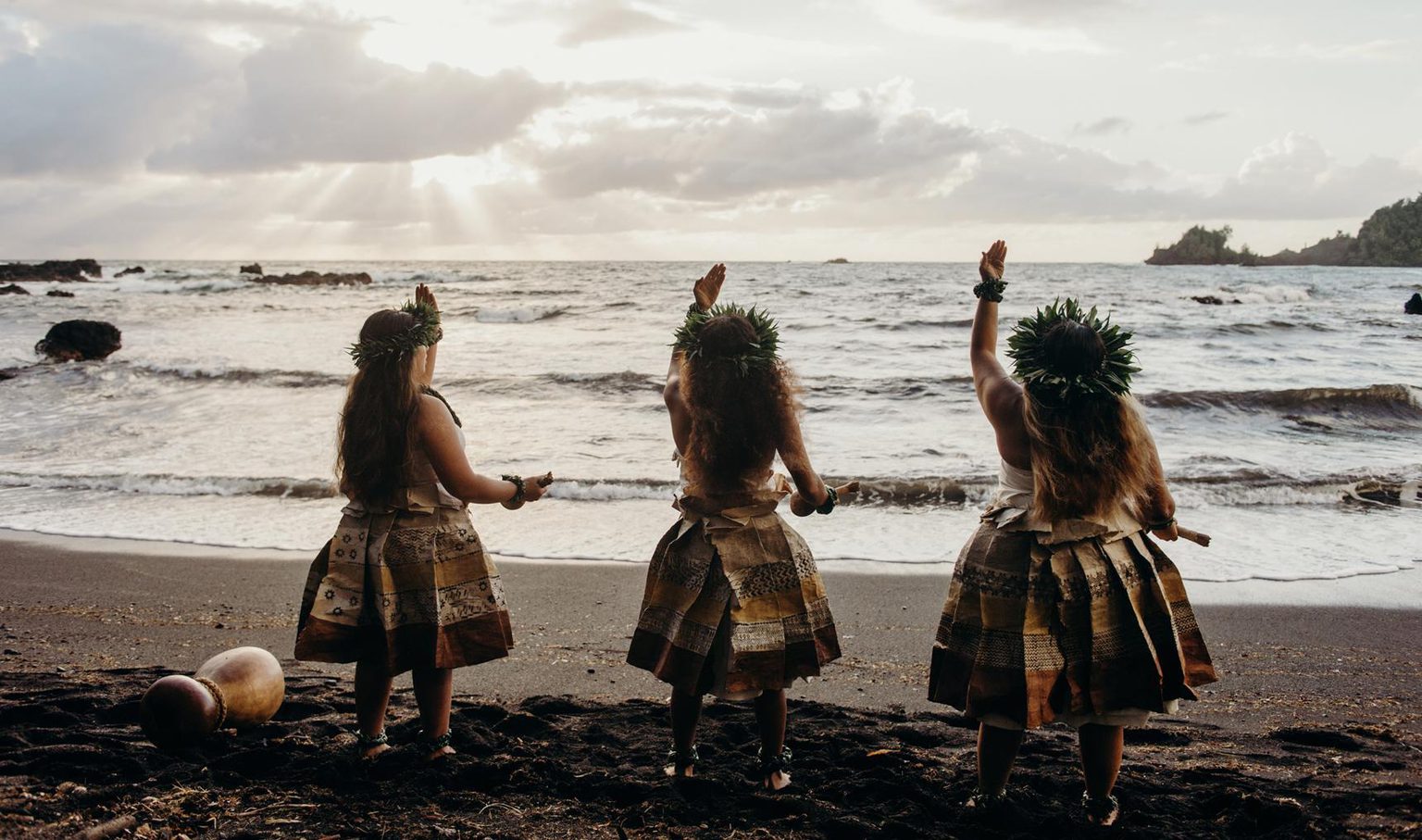 Three women dancing hulu on the beach at sunset