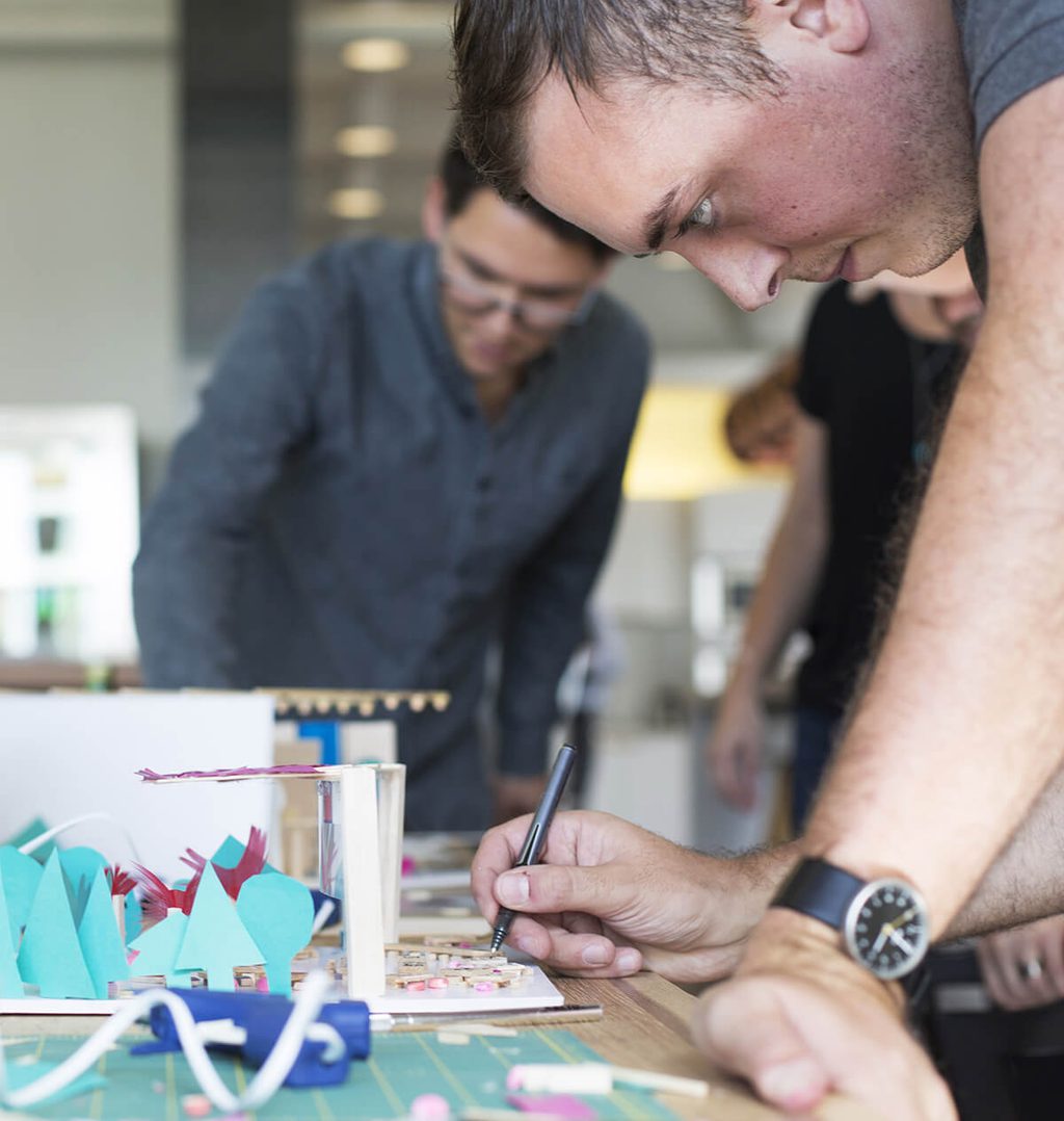 Man with black watch drawing next to a colorful 3D scale model of an interior space