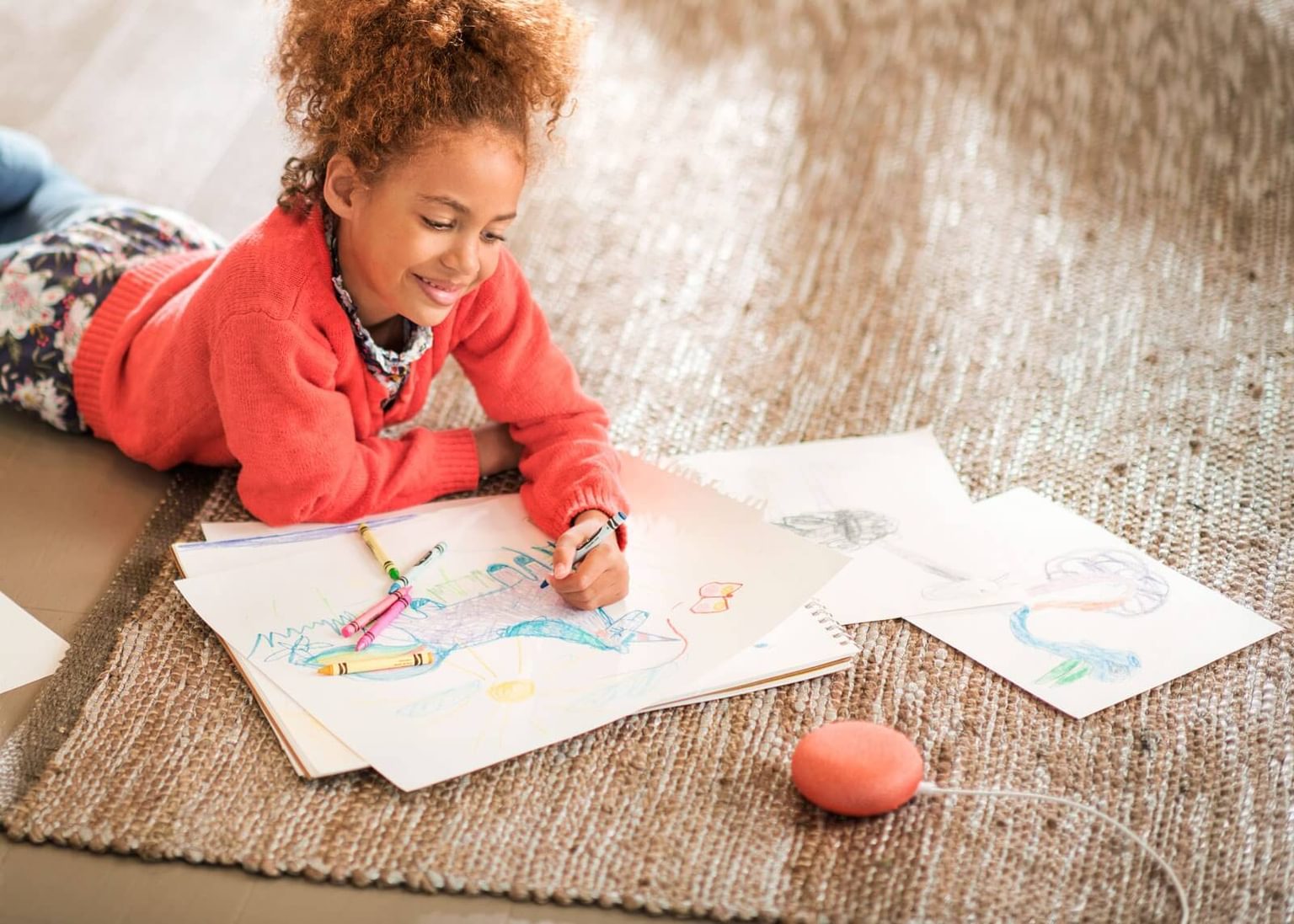 Child laying on carpet drawing next to a Google Home Mini device