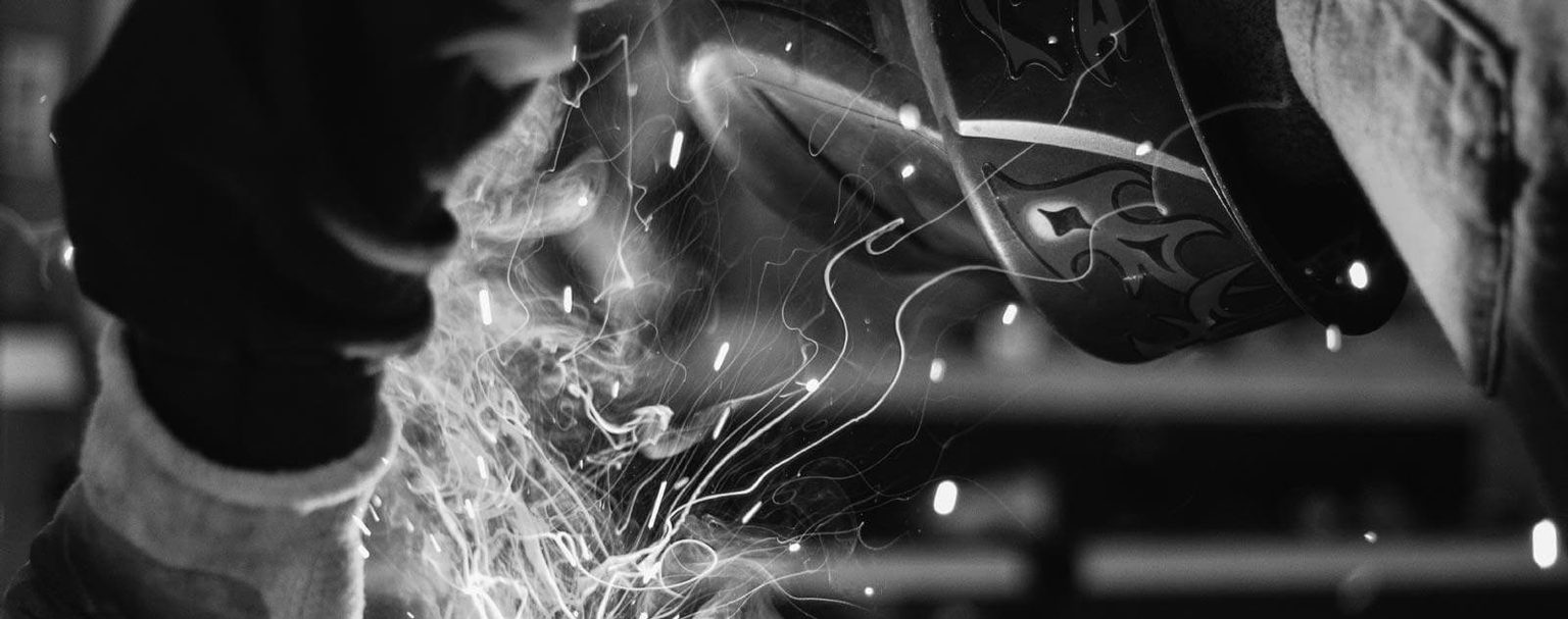 Man in welding helmet in protective gloves welding material with sparks flying