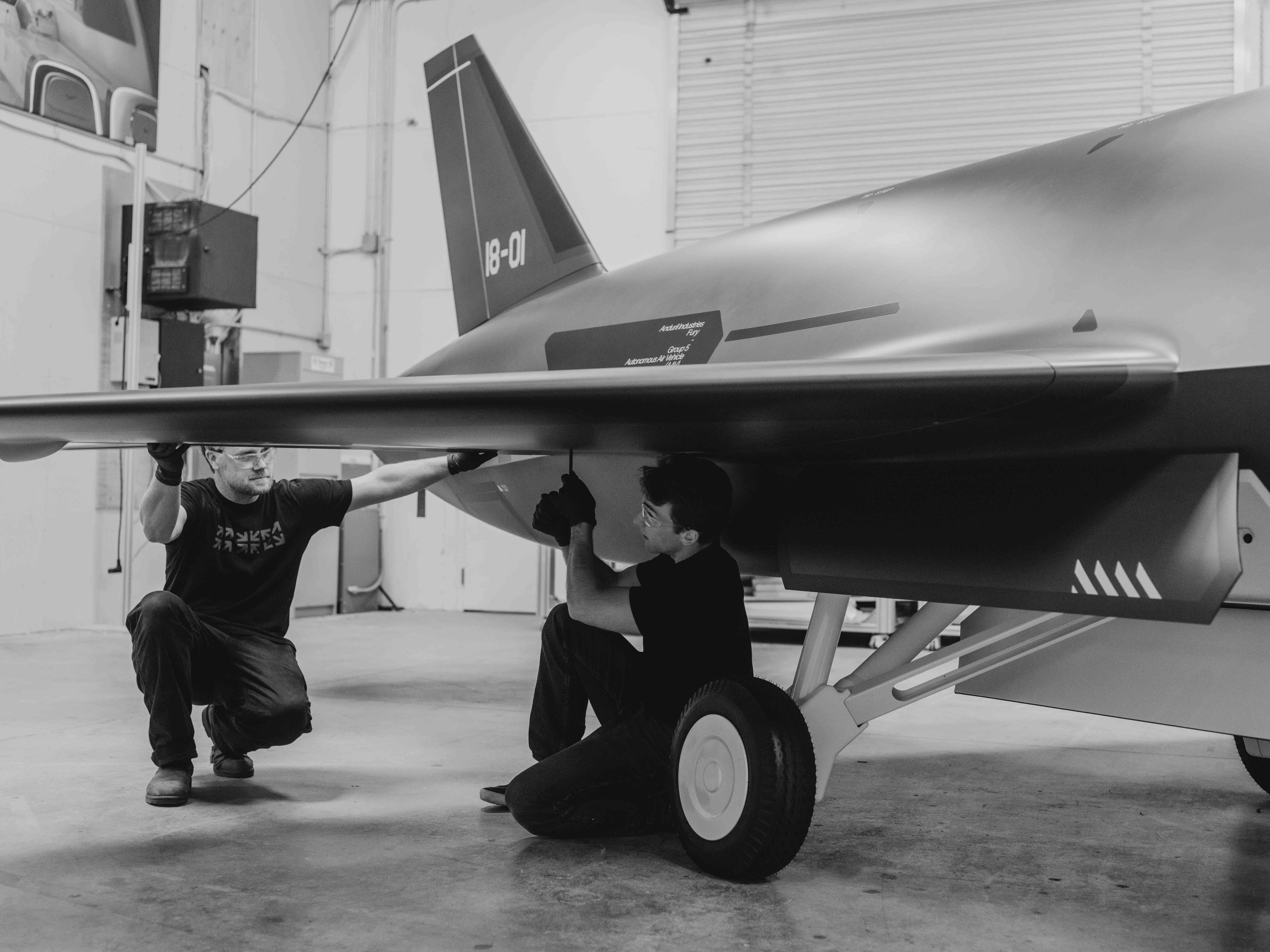 Two men kneeling next to aircraft mockup attaching wing