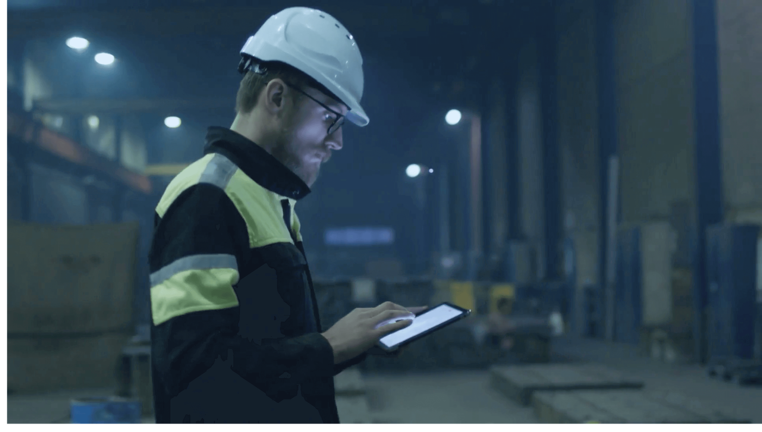 Man in hard hat walking through warehouse looking at a tablet