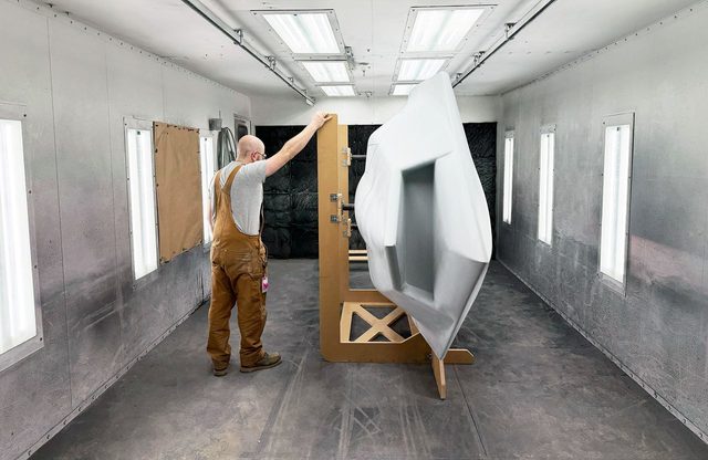 Man is brown overalls standing in large paint booth next to VTOL jet model