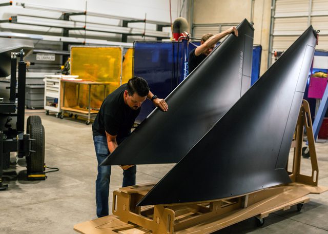 Two men handling aircraft wing mockups on a cart in a woodshop