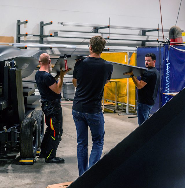 Three men in black attaching an aircraft model wing to the fuselage