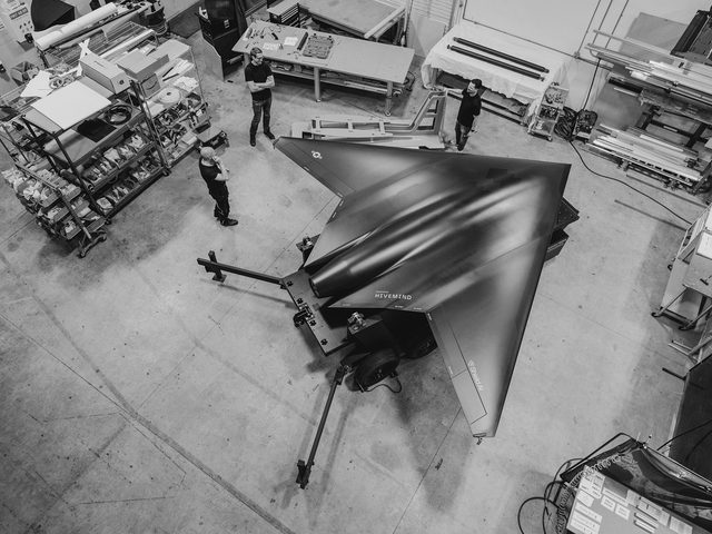 Top view of three men standing around a large black aircraft model