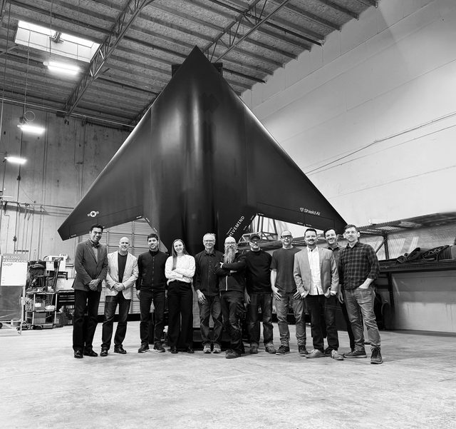 Large group of people standing in front of a VTOL fighter jet model vertically positioned