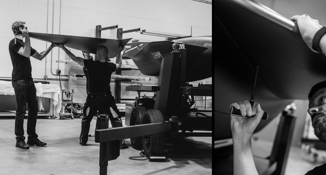 Three men in black positioning an aircraft wing onto a VTOL jet model