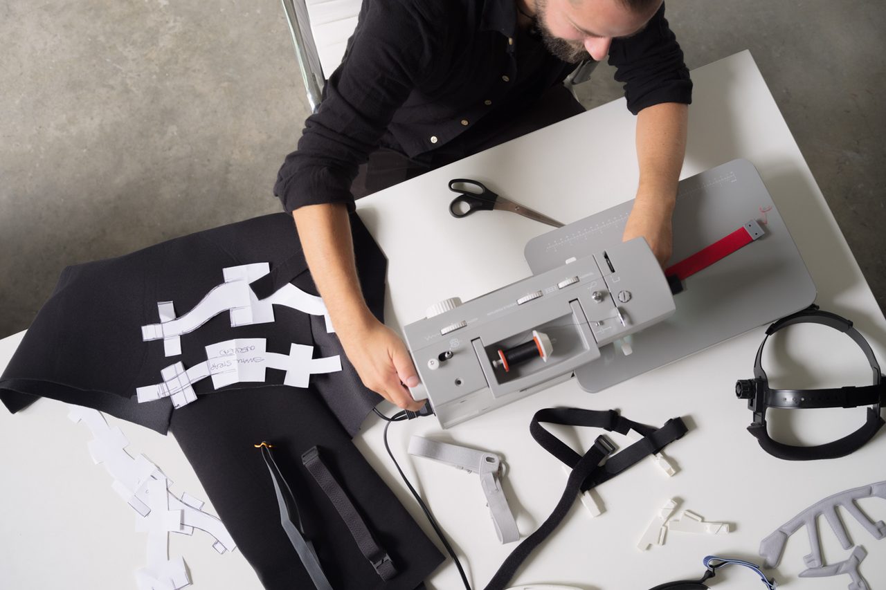 Man seated at table with a sewing machine and fabrics laid out
