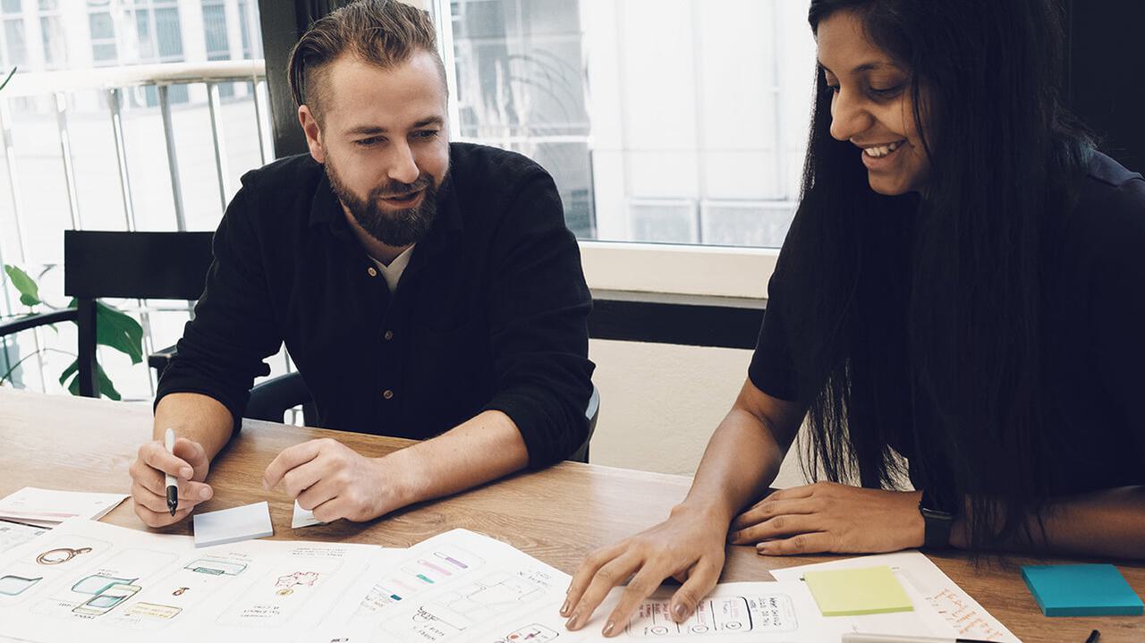 Man and women sitting at wood table in black shirts review user interface designs