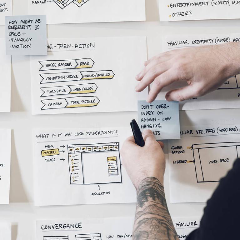 Man with arm tattoo sleeve attaching blue post it notes to whiteboard