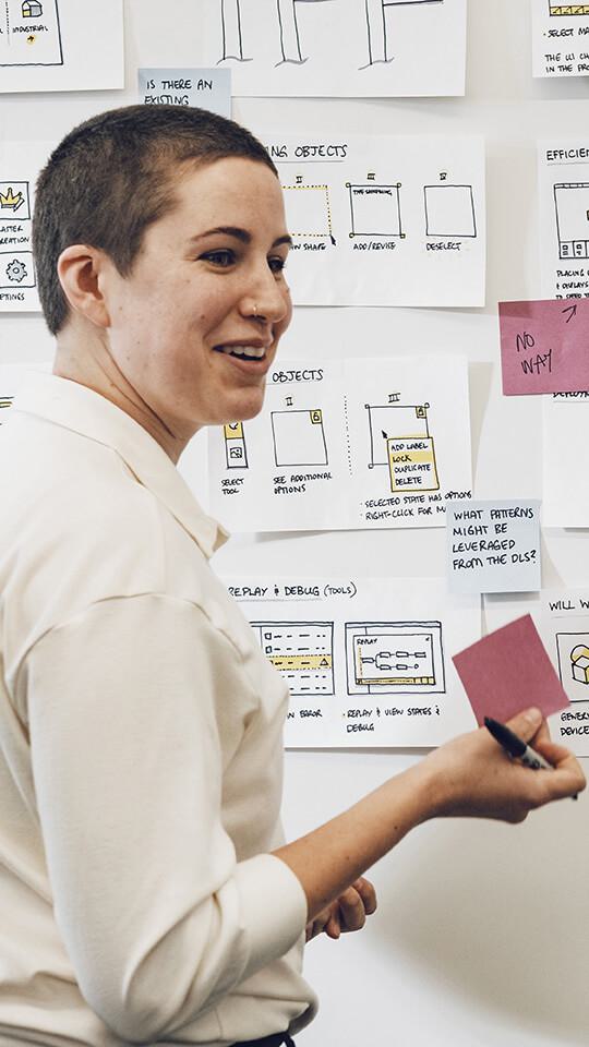 Person standing at whiteboard in white shirt holding purple post it notes