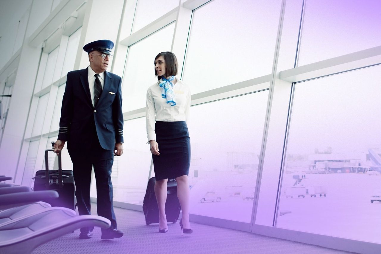 Pilot and flight attendant talking through airport with rolling bags