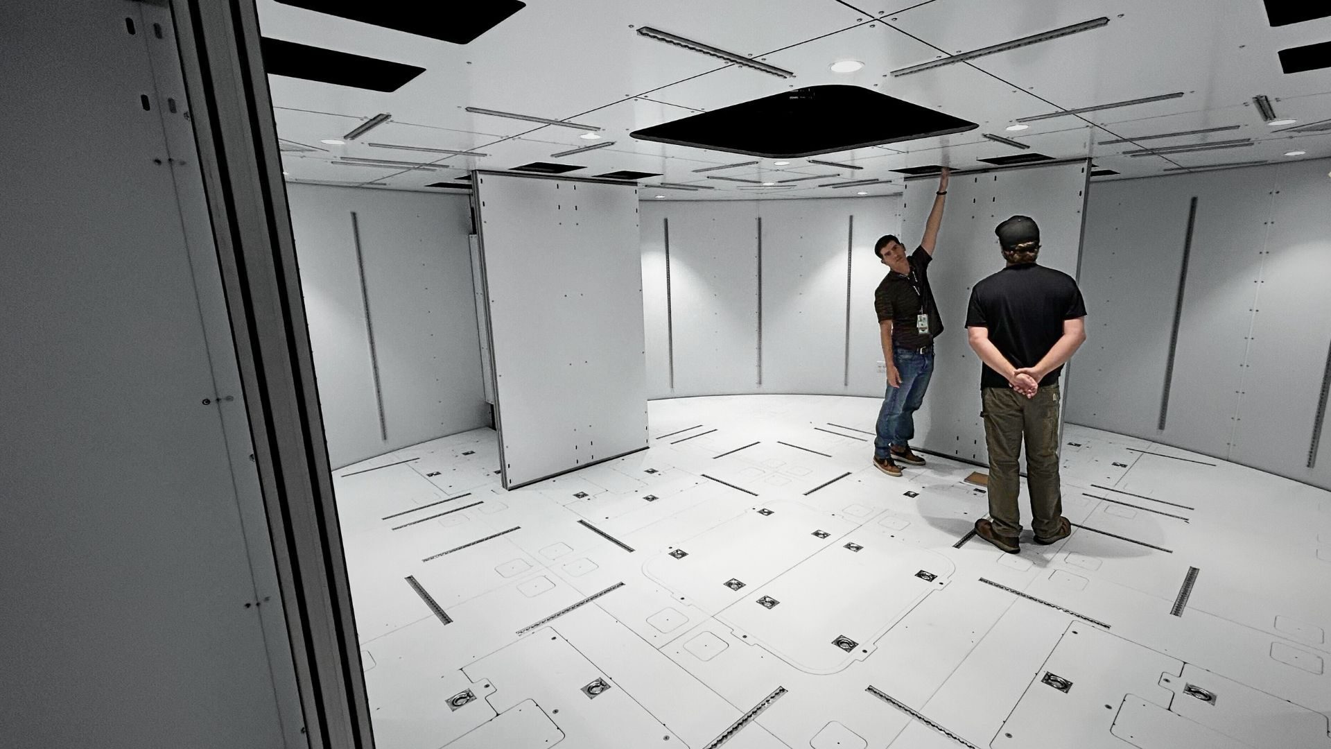 Two men standing inside a large scale mockup of a space station
