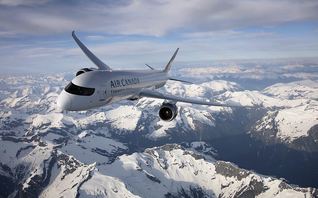 Air Canada 787 flying through the sky with snow capped mountains in the background