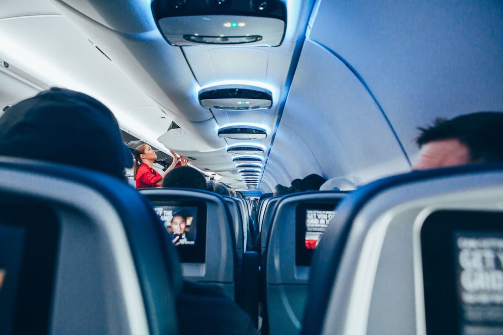 Flight attendant closing the overhead bin on a small airplane with blue lighting