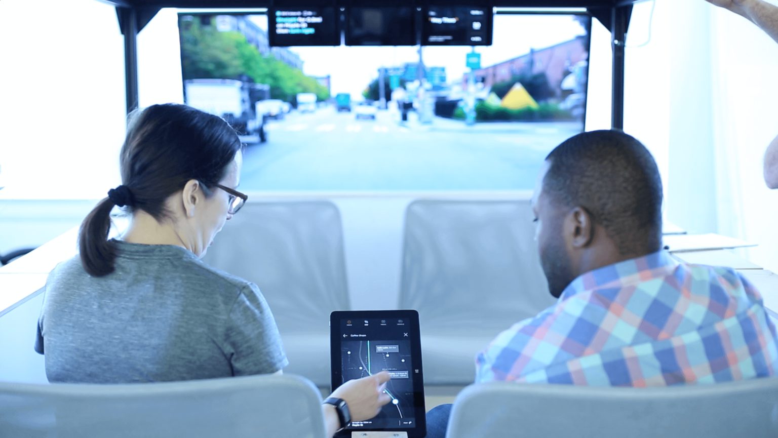 Two people sitting in mockup of an autonomous car testing an application on a tablet