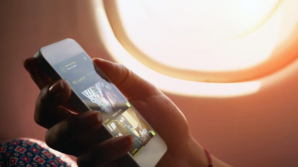 Women holding smart phone while seated next to a window in an airplane