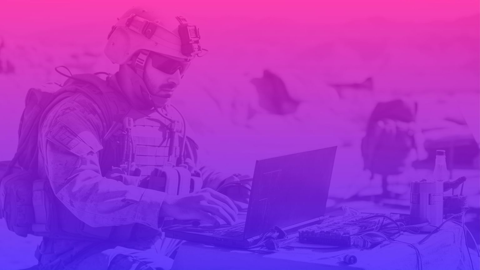 Soldier in combat gear sitting down working on a laptop in the desert