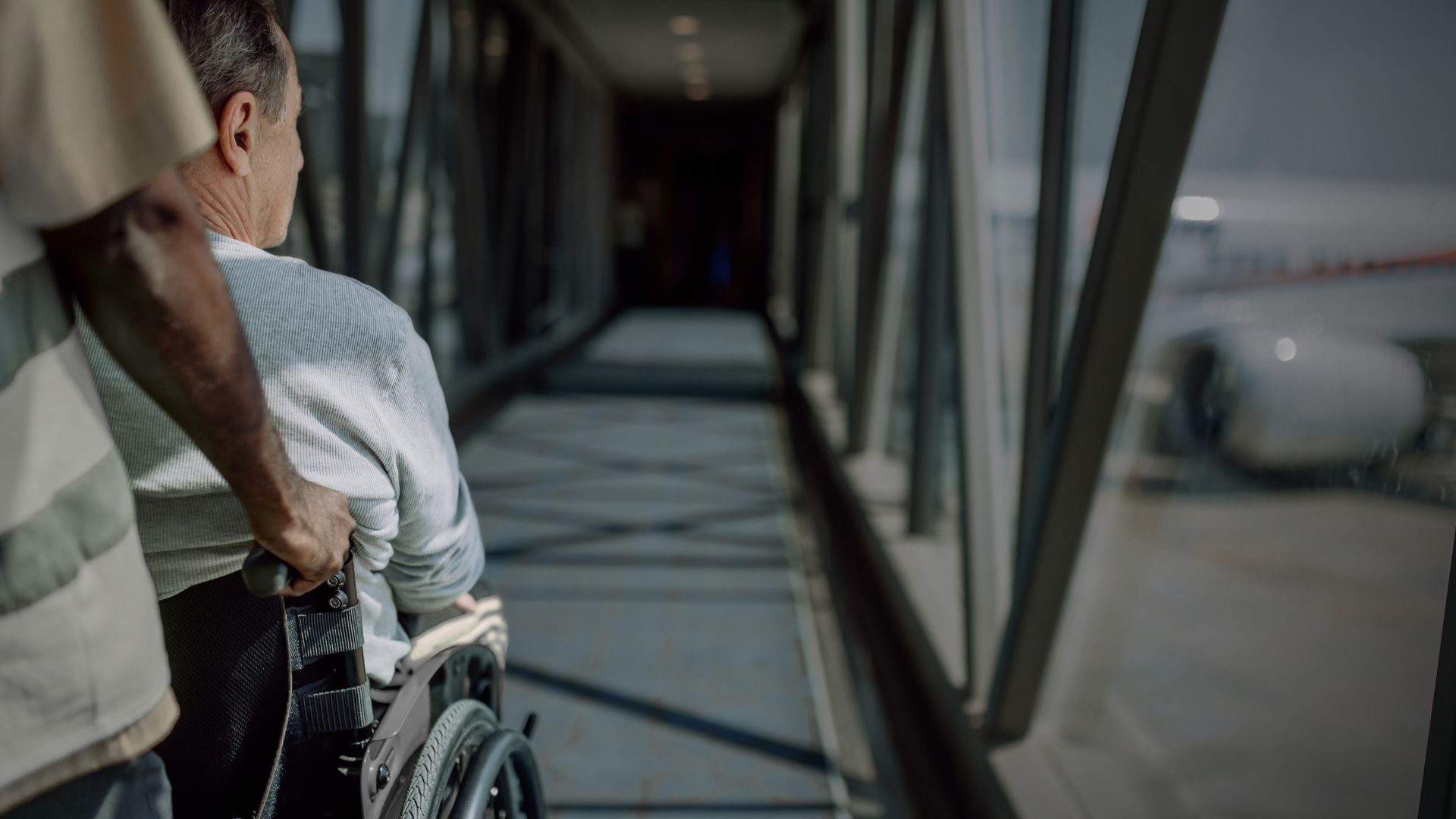 Man in wheelchair being escorted down jetway